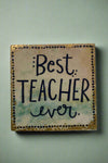 A small square sign that says “Best Teacher Ever” in black writing.