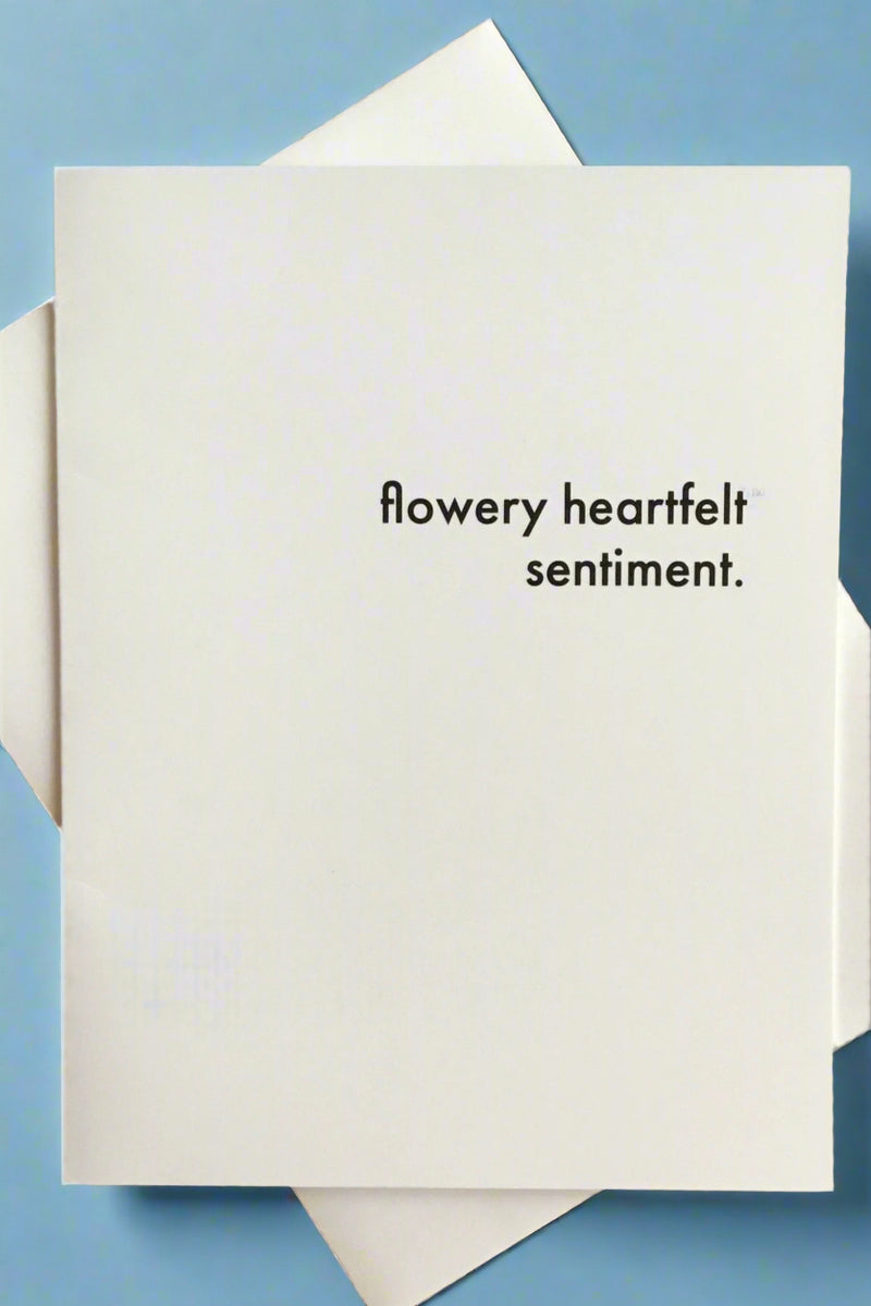 A solid white greeting card with small black text that reads ‘flowery heartfelt sentiment.’