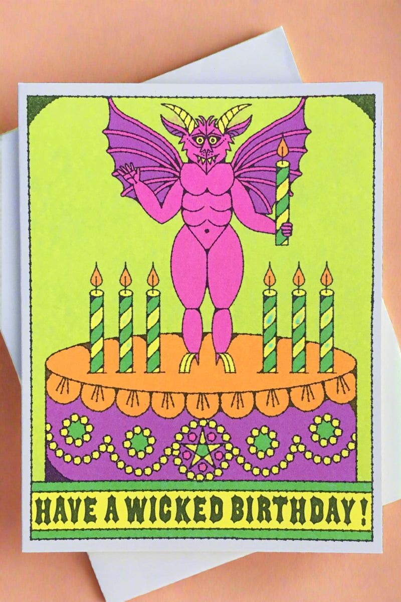 A greeting card with the image of a devilish monster standing on a birthday cake and text that reads ‘Have A Wicked Birthday!’