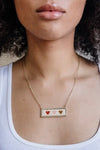 Dainty gold chain necklace with a beaded bar pendant with three different colored hearts.