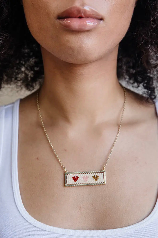 Dainty gold chain necklace with a beaded bar pendant with three different colored hearts.