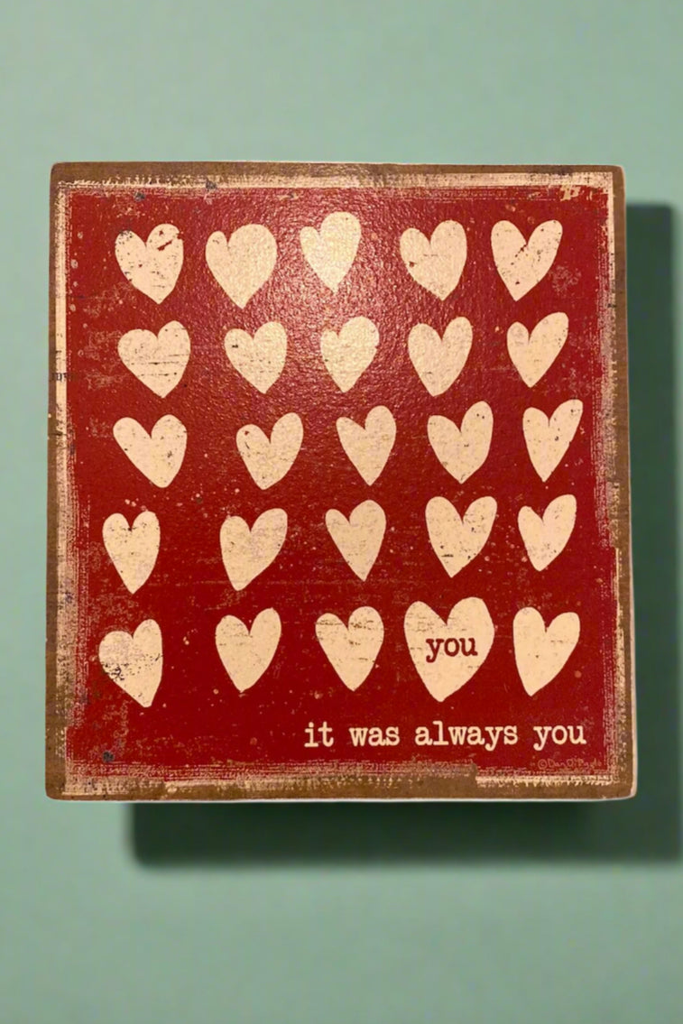 A square wood sign that has “It Was Always You” and hearts on the front.