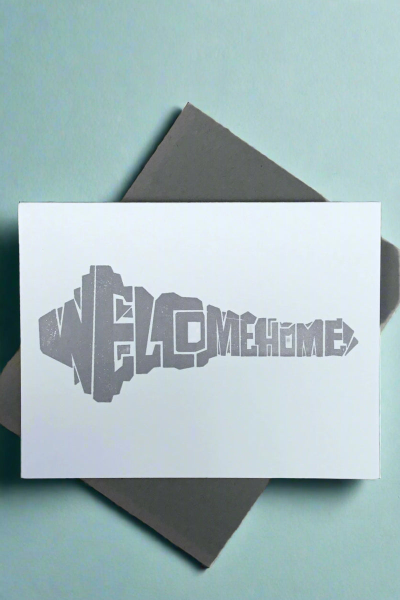 A white minimalist greeting card that says “Welcome Home” in the shape of a key.