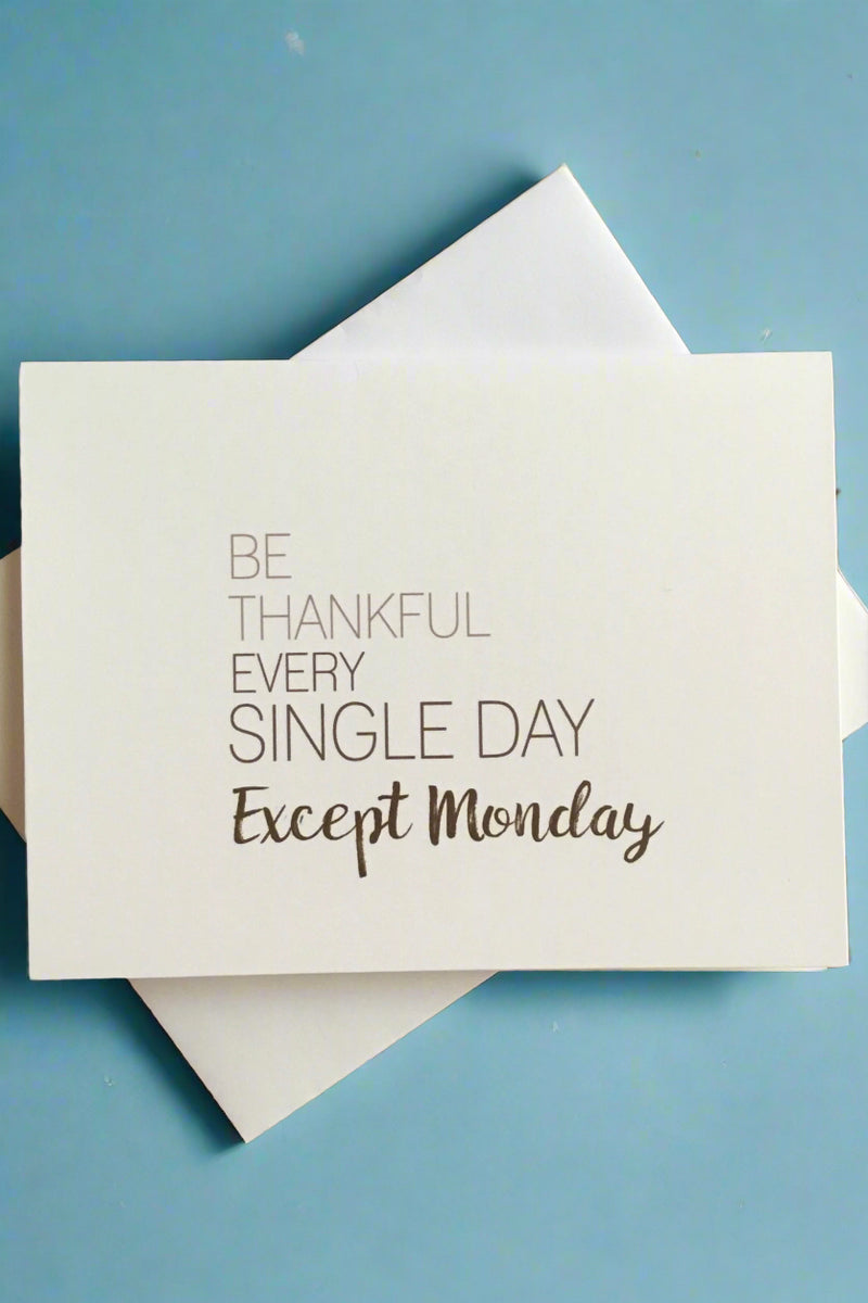 A white greeting card with text that reads ‘Be Thankful Ever Single Day Except Monday.’