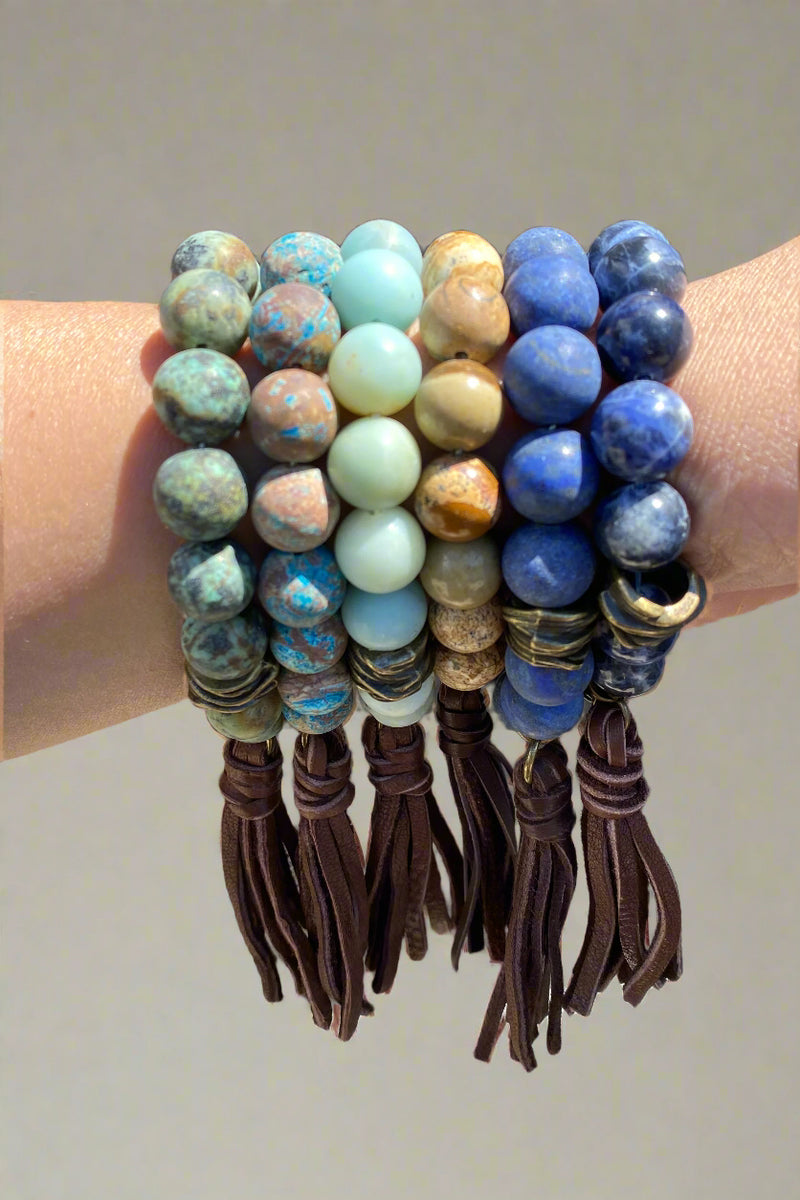 Model showcases various stone bracelets in turquoise, natural, and matte blue, featuring brass hardware and a real leather tassel.