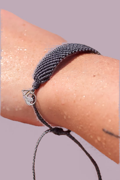 Grey woven bracelet with adjustable slider and small silver 4ocean charm. 
