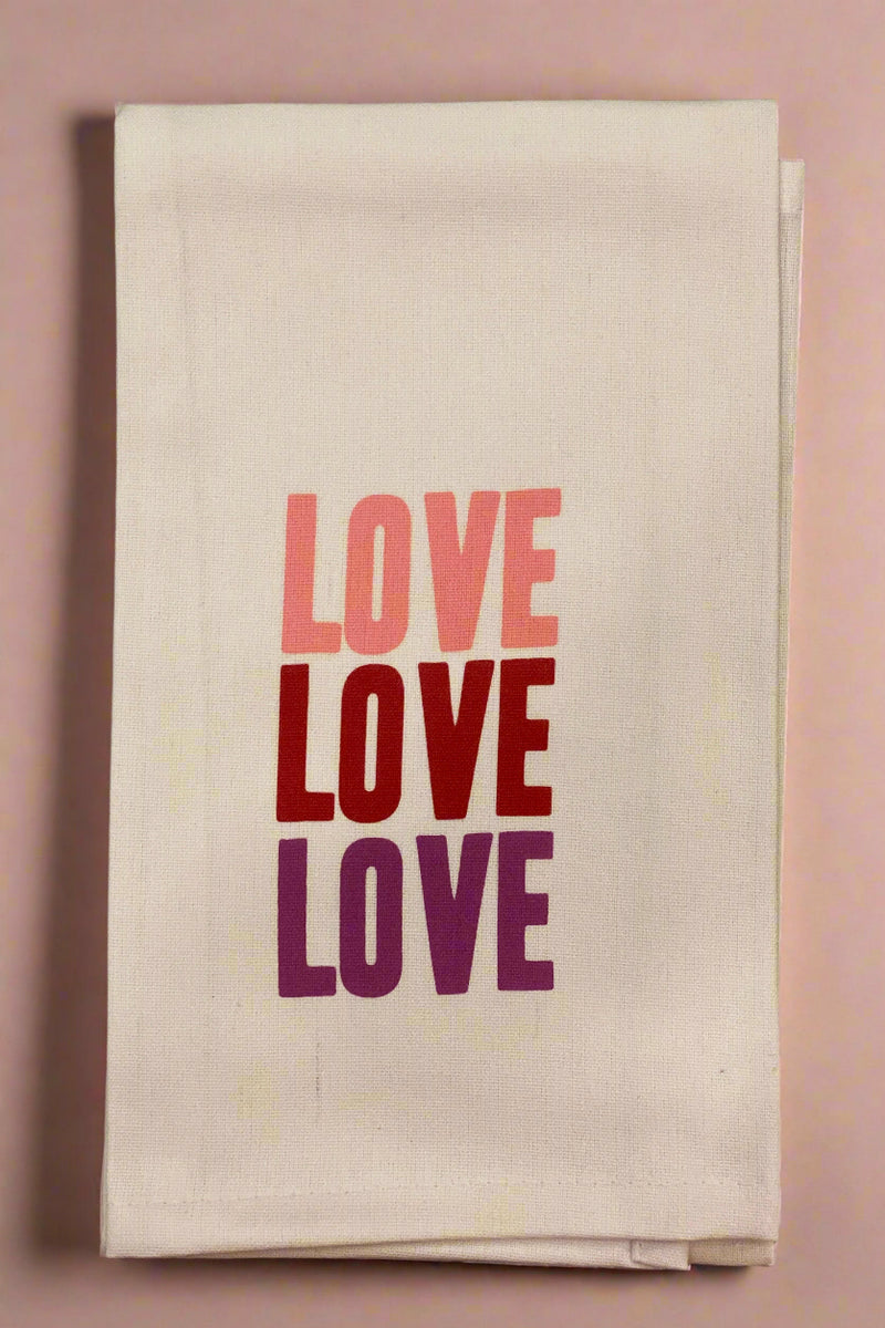 A tan, 100% cotton dish towel that has LOVE one the front in 3 different pink or red colors.