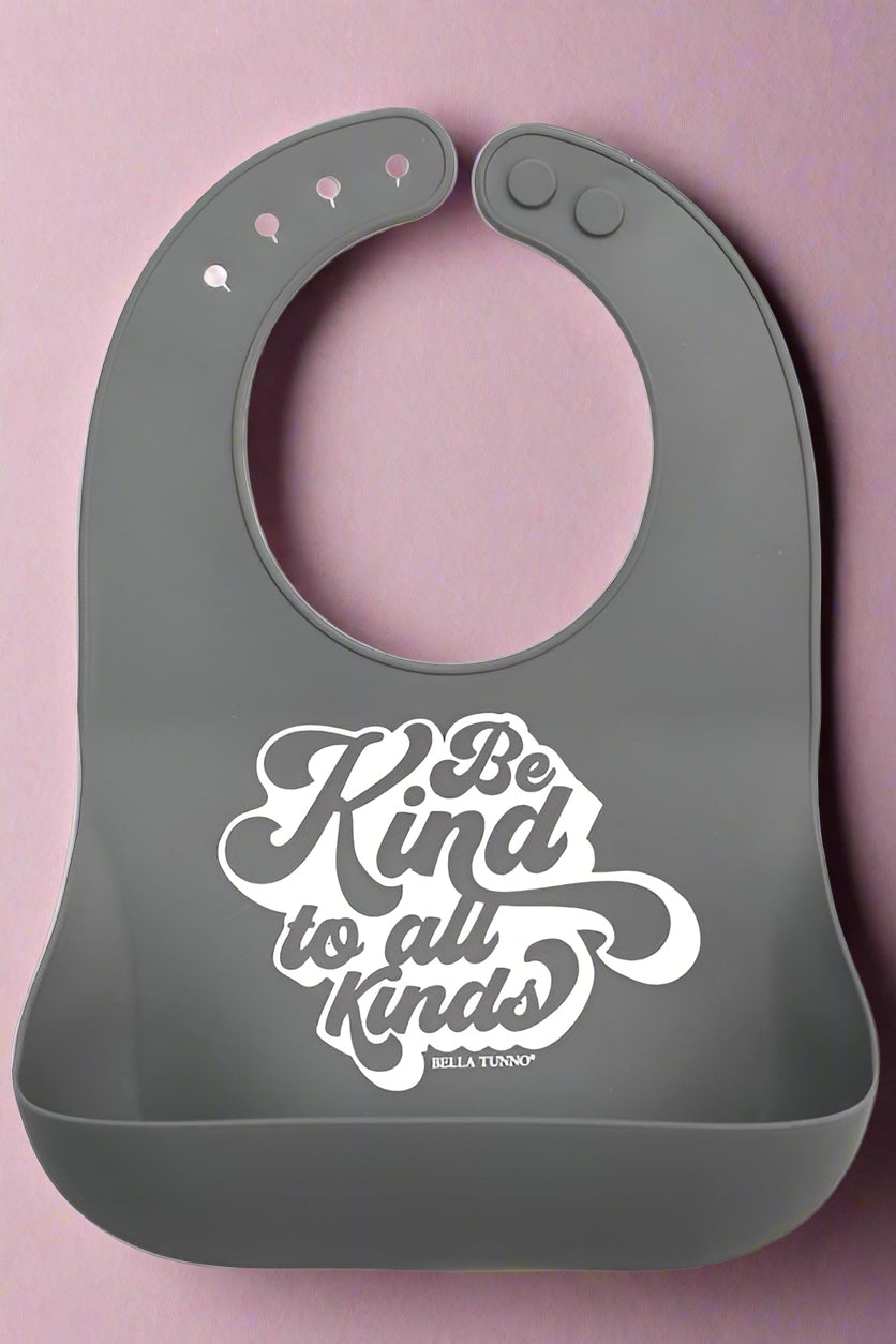 A grey adjustable neck bib with a the phrase Be Kind To All Kinds. Recommended for kids 6 months+.