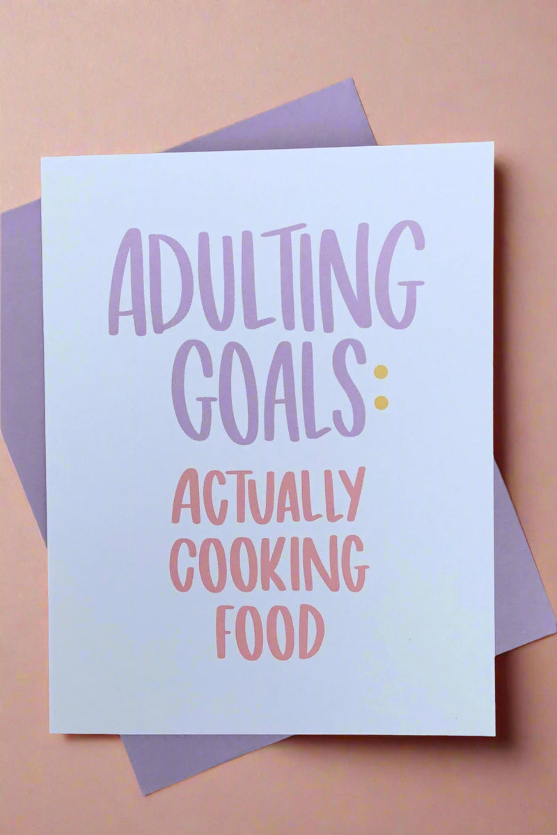 A white card that says “Adulting Goals: actually cooking food” in purple and pink.