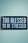 A black rectangle sign that says “Too blessed to be stressed” in white.