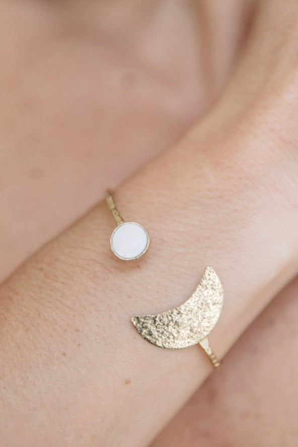 A wrist cuff of textured brass with a crescent moon and pearl accent.