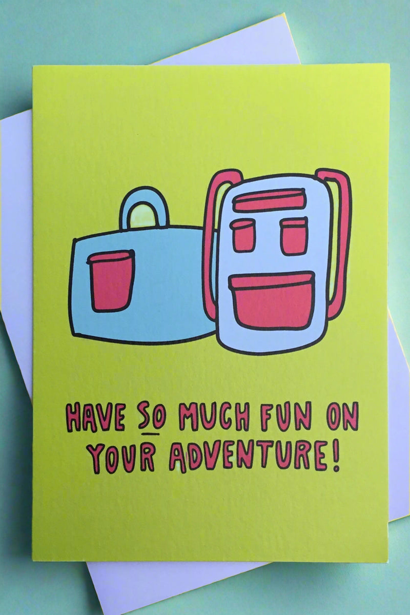 A bright green greeting card with the image of a backpack and suitcase and red text that reads ‘have SO much fun on your adventure!’