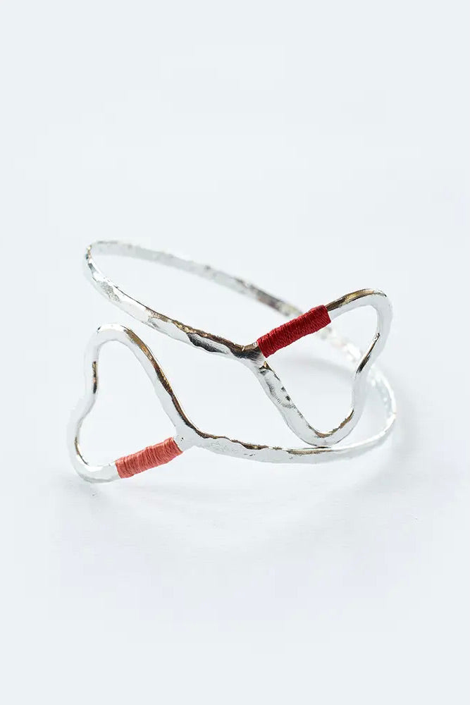 Open, silver-toned, bangle featuring two large hearts and pink and red thread.
