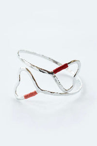 Open, silver-toned, bangle featuring two large hearts and pink and red thread.