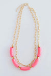 The Holly necklace is layered with a shorter, chain link pattern while the longer chain is strung with several pink, elongated beads.