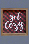 A small wood framed sign that has a red and black checkered background and “get cozy” written in white.