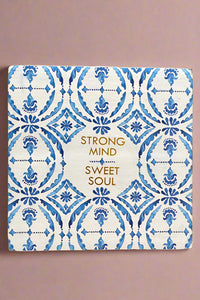 A small square sign with a white and blue pattern and says “Strong mind, sweet soul” written in gold.