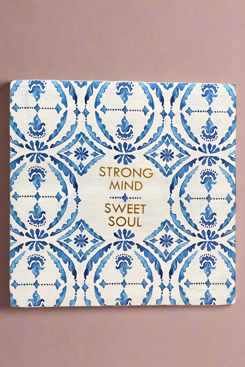 A small square sign with a white and blue pattern and says “Strong mind, sweet soul” written in gold.