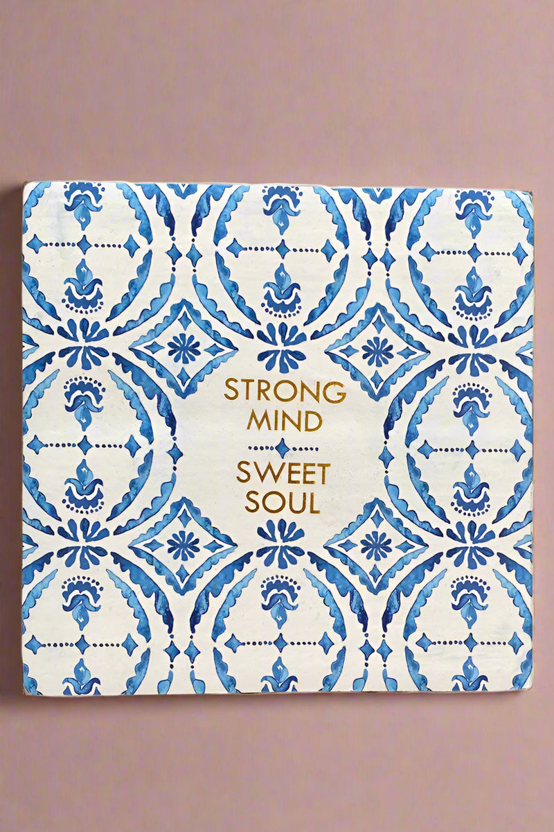 A small square sign with a white and blue pattern and says “Strong mind, sweet soul” written in gold.