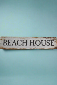 A aged white wood sign that says Beach House on the front.