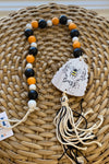 Black, white and orange wooden bead garland with a beehive shaped ornament and tassel at the end.
