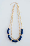 The Holly necklace is layered with a shorter, chain link pattern while the longer chain is strung with several royal blue, elongated beads.