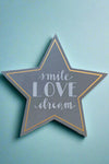 A dark grey star shaped sign that says “Smile, love, dream.”