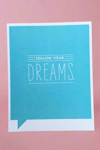 A greeting card with bright blue background and white text that reads ‘Follow your Dreams.’