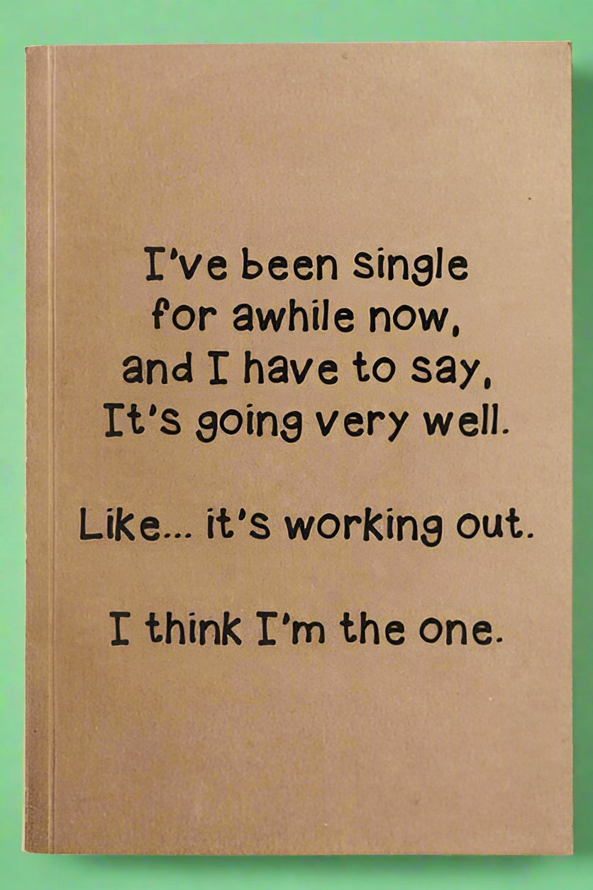 A notebook with lined paper and brown kraft paper cover that reads “I’ve been single for awhile now, and I have to say, it’s going very well. Like… it’s working out. I think I’m the one.”