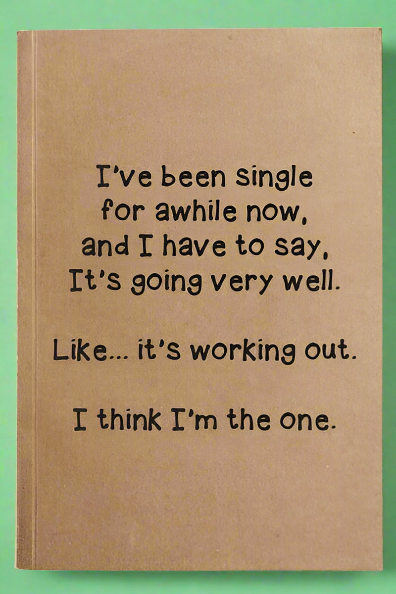 A notebook with lined paper and brown kraft paper cover that reads “I’ve been single for awhile now, and I have to say, it’s going very well. Like… it’s working out. I think I’m the one.”