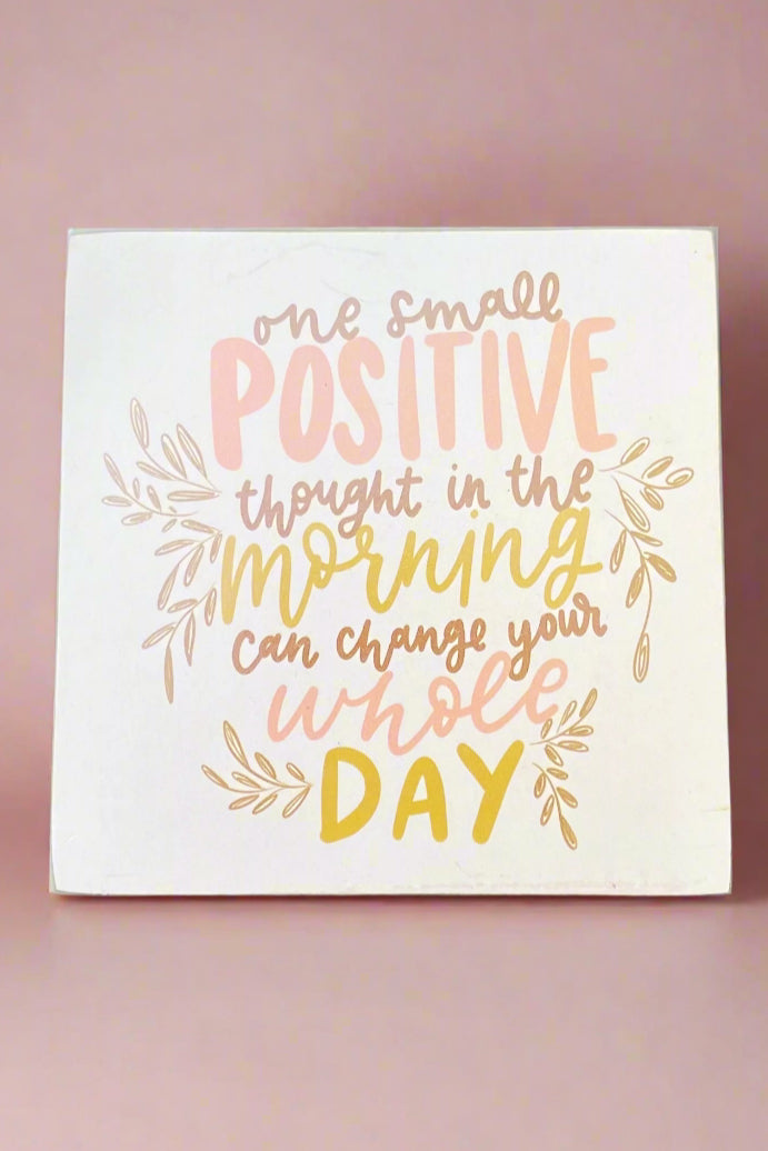 4 inch solid wood block sign painted white with “one small positive thought in the morning can change your whole day” written in pastel pink and yellow.