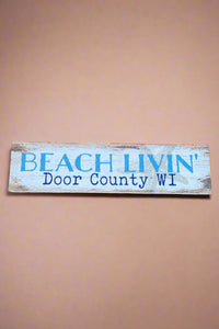 A horizontal rectangle sign in rustic white that says “Beach Livin’ Door County Wi.”