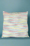 A square accent pillow with exposed multicolored stitching.