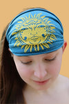Soft teal headband featuring a vibrant yellow sun printed across the front. 